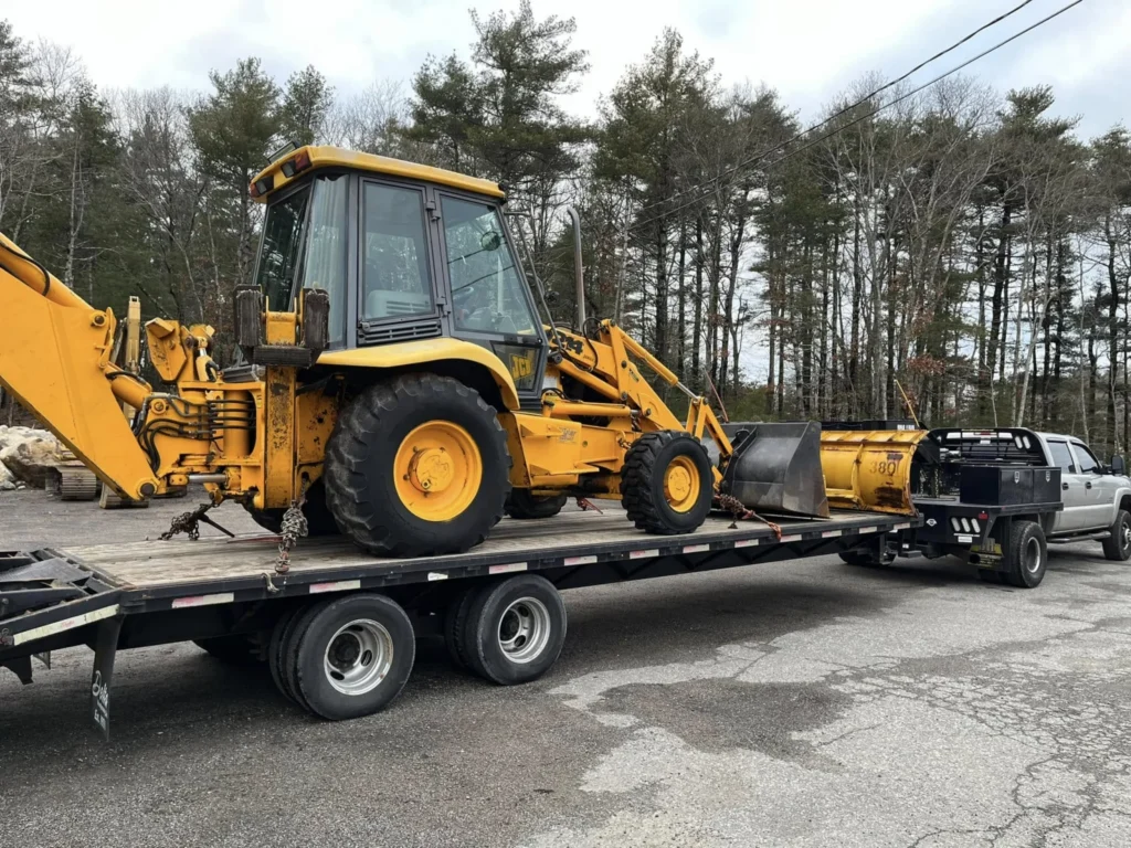 Yellow backhoe loader secured on a JP equipment trailer