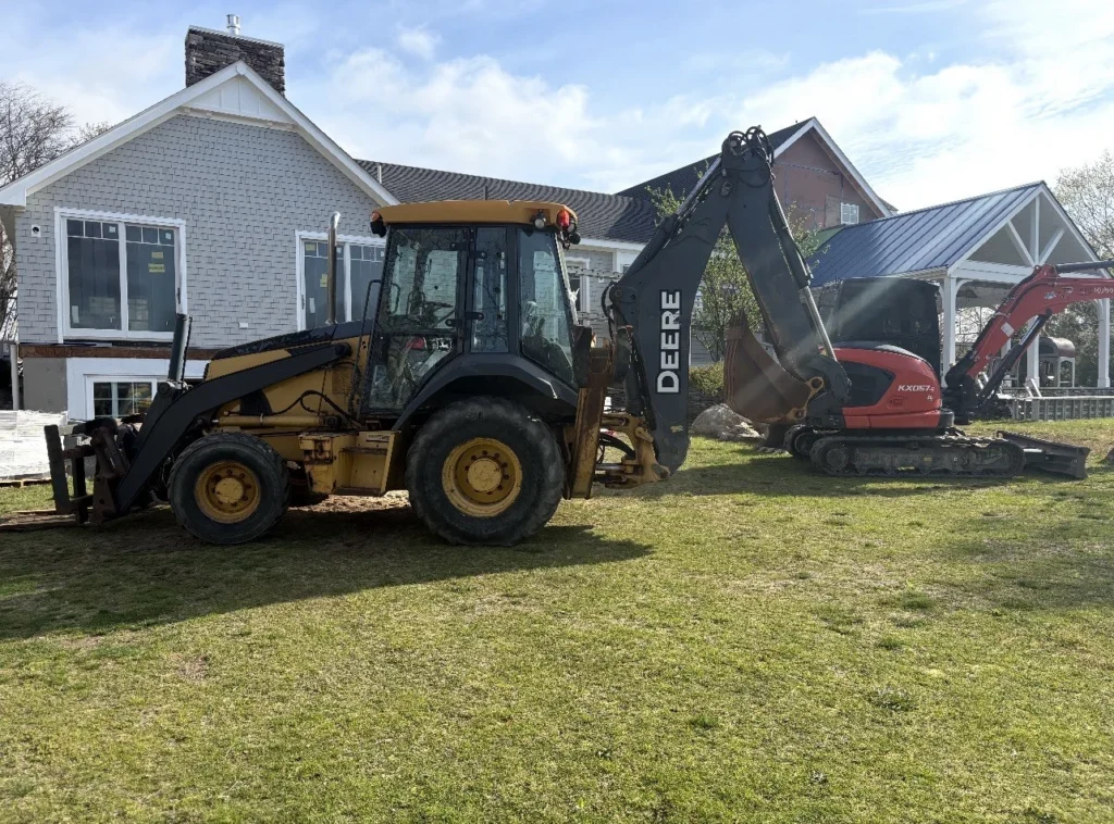 John Deere backhoe and Kubota excavator working at a residential property