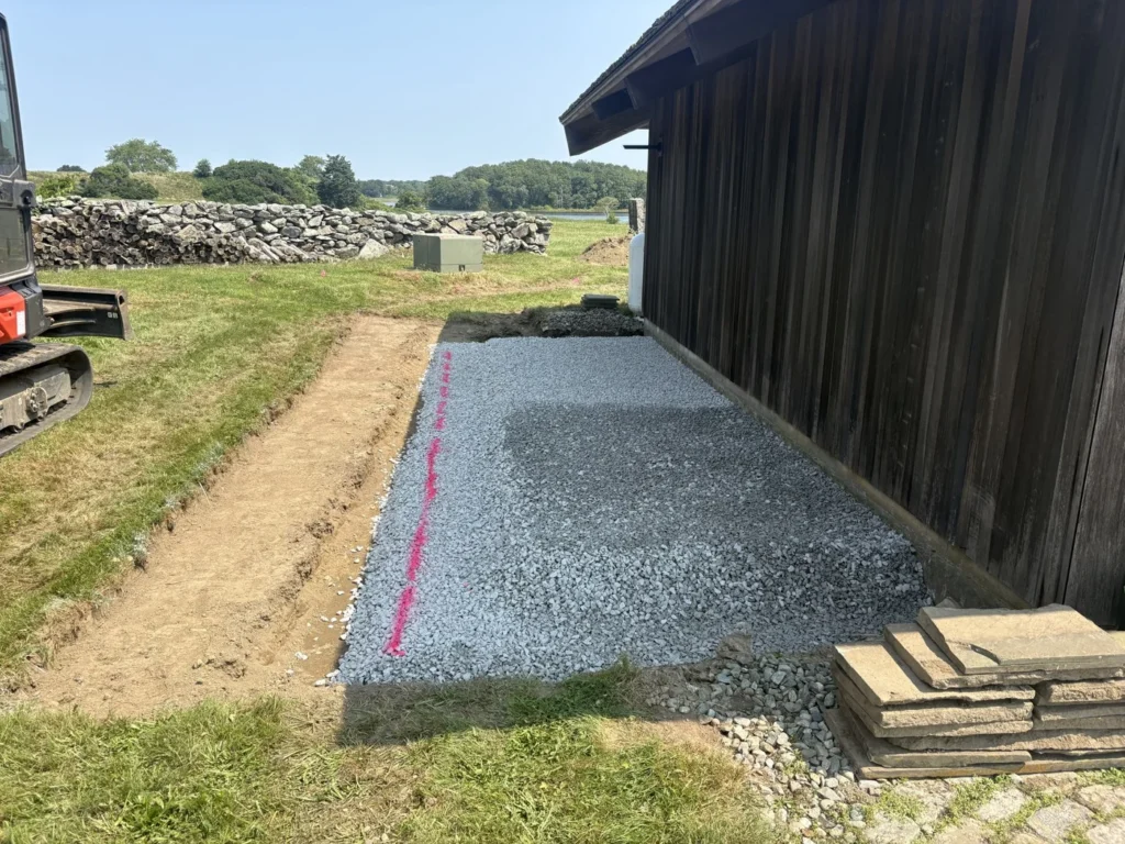 Aggregate base preparation beside a dark-sided building