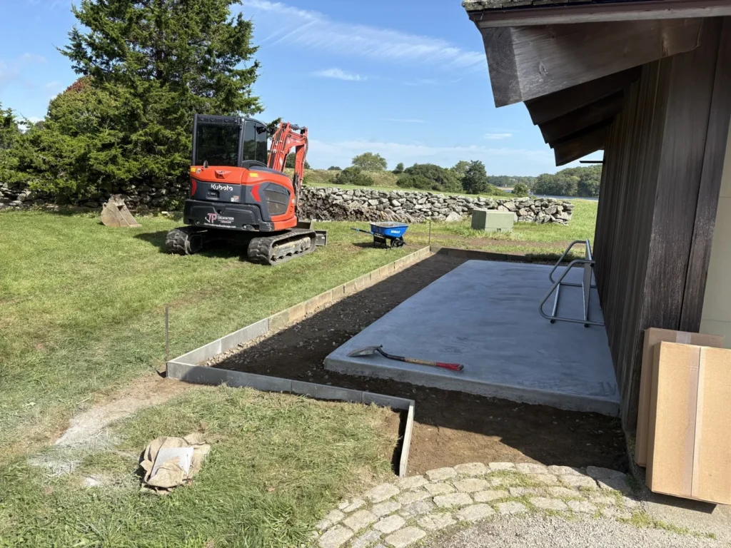 Compact excavator shaping an outdoor area beside a building