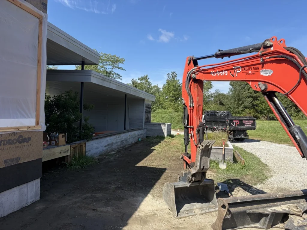 Orange Kubota excavator arm beside a JP dump truck at a work site