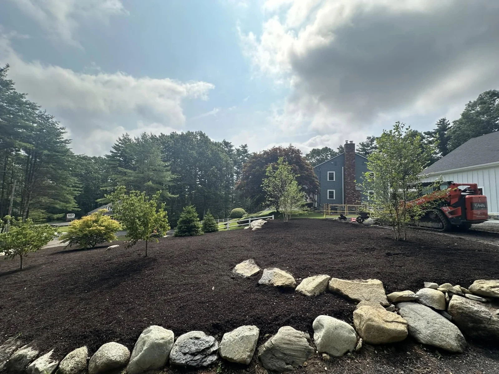 Fresh landscape preparation with boulder edging and a Kubota loader