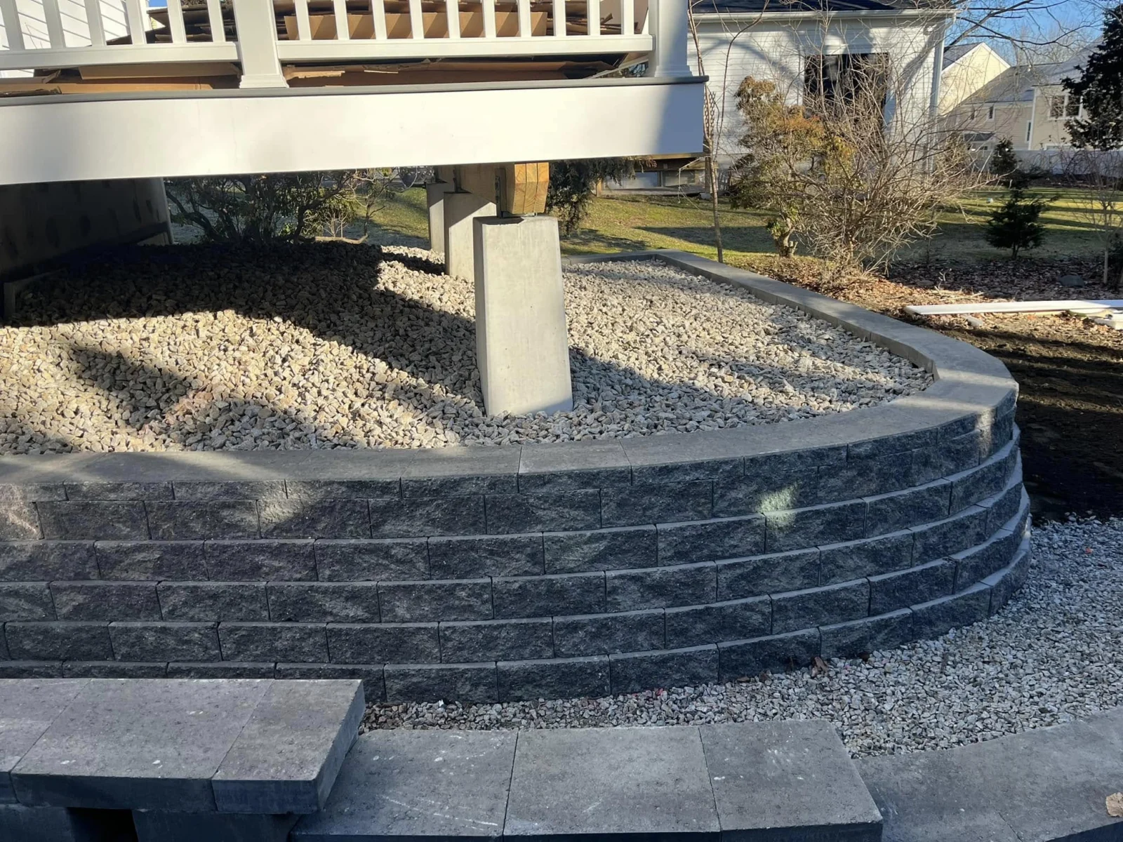 Curved block retaining wall and stone base beside a raised deck